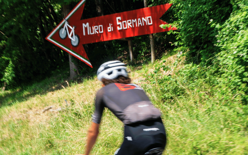 Ciclista pedala davanti al cartello che indica la salita al muro di Sormano durante un tour in bici da corsa di Joule